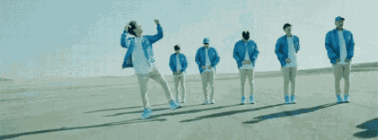 a group of young men in blue jackets are dancing on a dirt road .