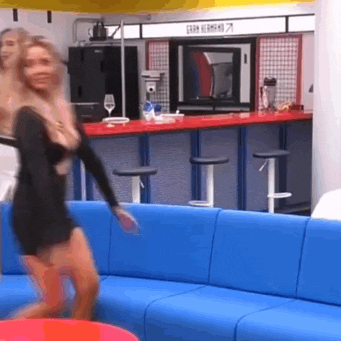 a woman in a black dress is dancing in a room with a sign that says gran hermano 7