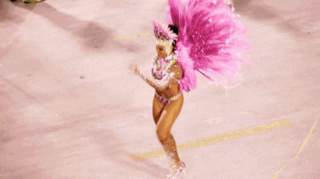a woman in a pink feathered costume is dancing in a crowd