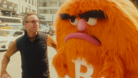 a man stands next to a stuffed animal with a letter b on its face