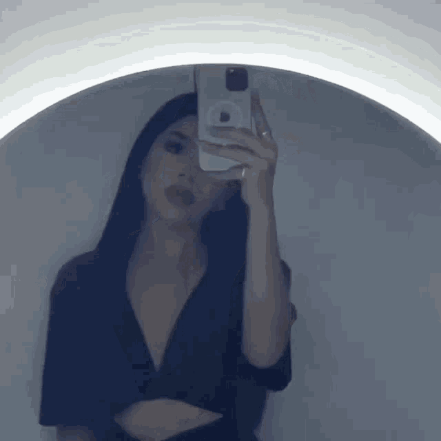 a woman is taking a selfie in front of a mirror with her phone .