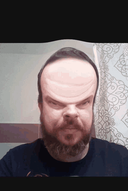 a man with a beard and a black shirt is making a funny face in front of a shower curtain