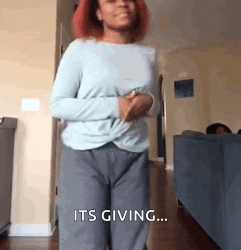 a woman in a blue shirt and grey pants is standing in a living room and says it 's giving ...