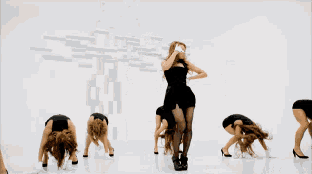 a group of women in short black dresses are dancing in front of a white wall