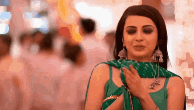 a woman in a green dress is standing in a crowded area with her hands on her chest .