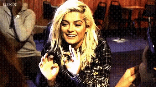 a blonde woman in a plaid shirt is smiling and clapping her hands