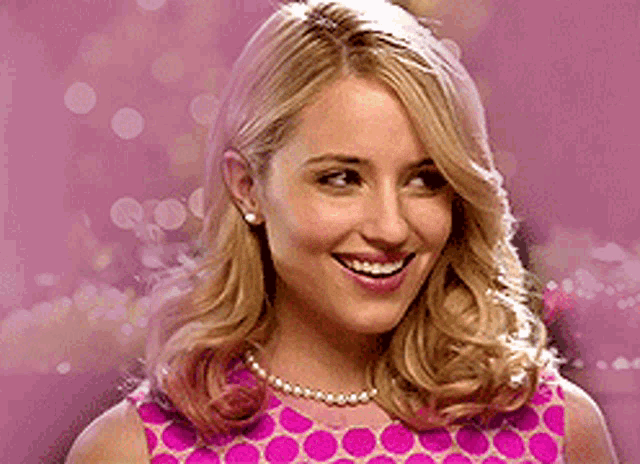 a woman wearing a pink polka dot dress and pearls smiles