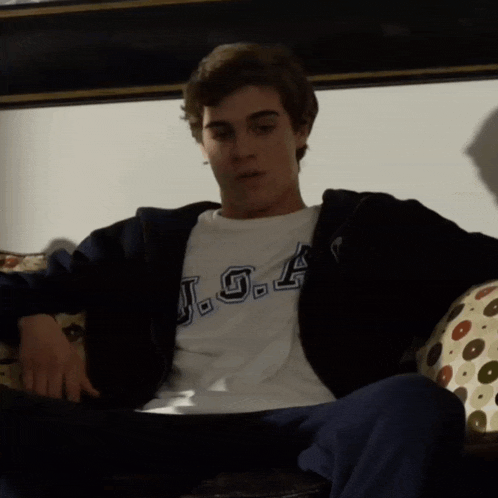 a young man is sitting on a couch wearing a j.g.a. shirt