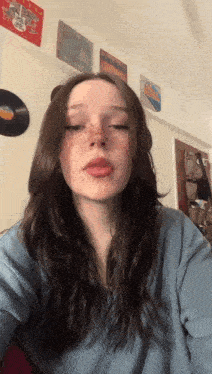 a girl with freckles on her face is wearing a blue sweater and taking a selfie .