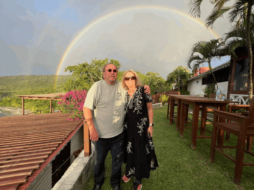 a man and a woman are posing for a picture under a rainbow