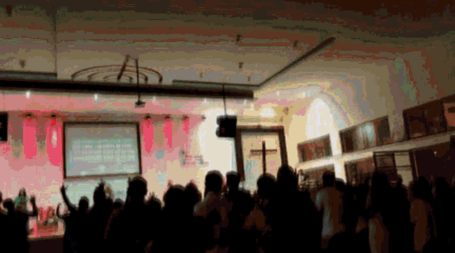 a crowd of people are gathered in a room with a large screen behind them that says ' a ' on it