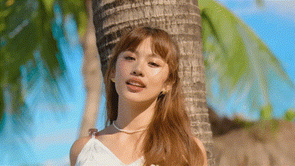 a woman in a white dress is leaning against a palm tree on the beach .