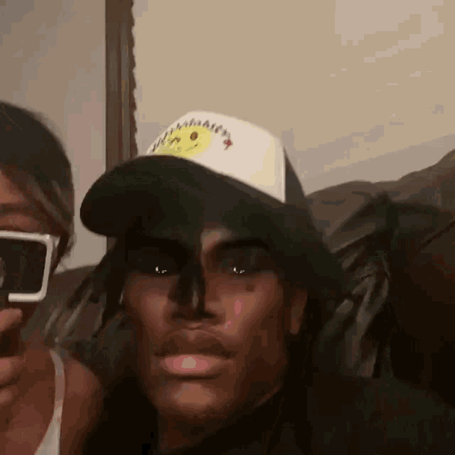 a man wearing a hat with a smiley face on it is taking a picture of himself .
