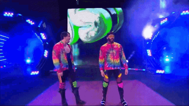 two men in tie dye shirts are walking down a runway