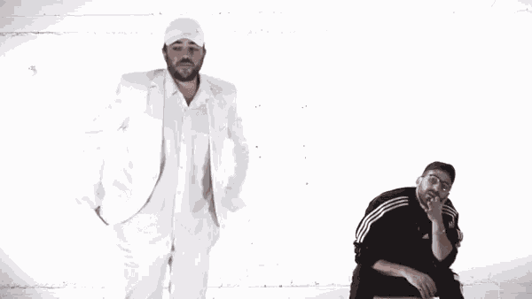 a man in a white suit stands next to another man in a black adidas jacket