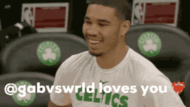 a man wearing a celtics t-shirt is smiling while sitting in the stands .