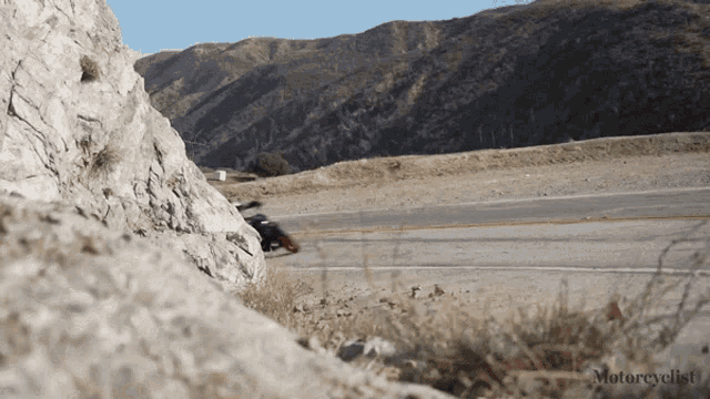 a motorcycle is going down a road with mountains in the background and the words motorcyclist on the bottom