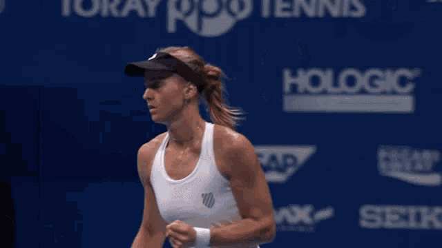 a woman in a white tank top is playing tennis in front of a blue wall that says hologic