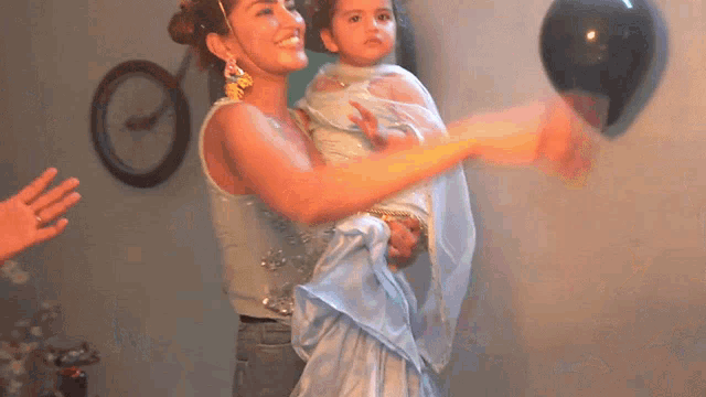 a woman is holding a little girl in her arms while holding a black balloon .