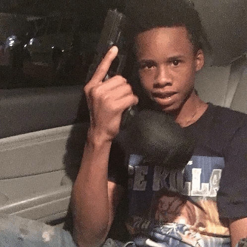 a young man is holding a gun in his hand while sitting in the back seat of a car .