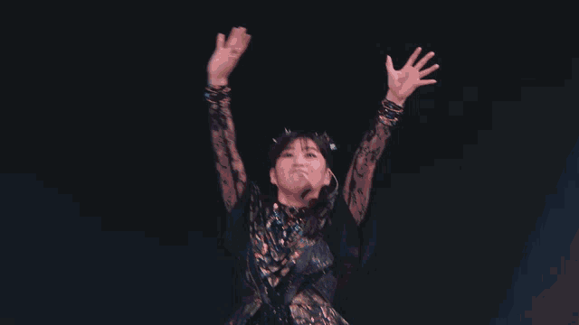 a woman in a black and gold dress holds her arms up in the air