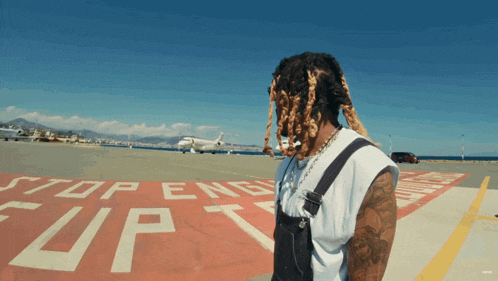 a man with dreadlocks stands on a runway with a stop sign on it