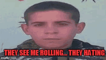 a young man is standing in front of a wall with the words `` they see me rolling ... they hating '' .