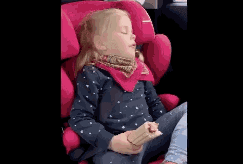 a little girl is sleeping in a car seat while holding a snack .