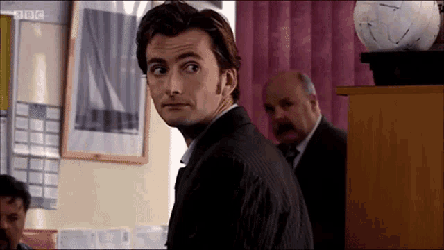 a man in a suit is standing in a room with a bbc logo in the corner