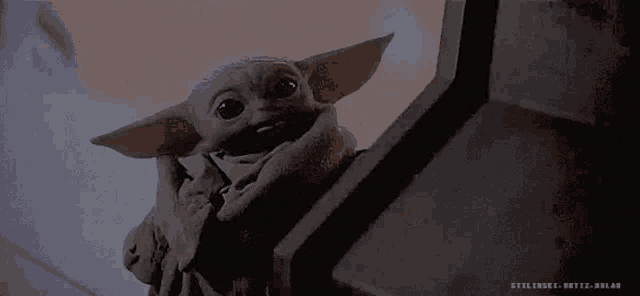 a baby yoda from star wars is sitting on a staircase looking at the camera .