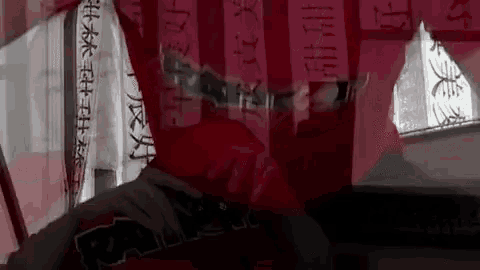 a person wearing a red raiders shirt is holding a knife in front of a wall with chinese writing on it .