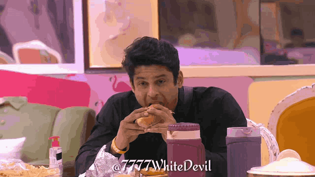 a man sitting at a table eating a hamburger with the words 7777 white devil written below him