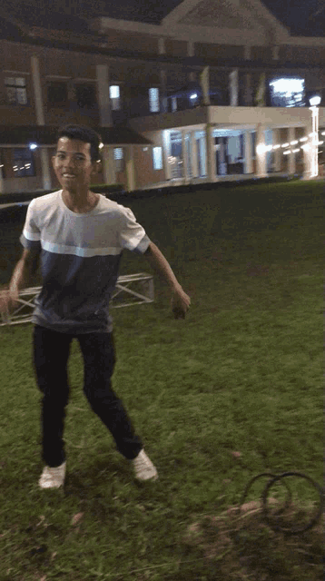 a boy in a blue and white shirt is dancing in a grassy field