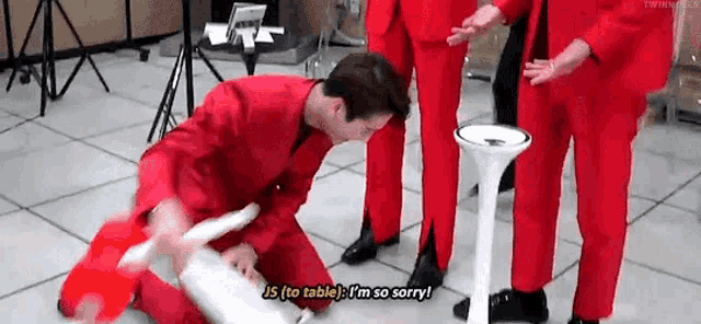 a man in a red suit is kneeling on the floor next to a table while holding a stick .