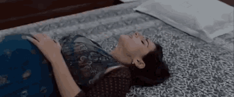 a woman in a blue dress is laying on a bed with her eyes closed .
