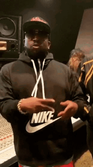 a man wearing a black nike hoodie stands in front of a piano