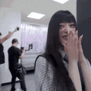 a woman covering her face with her hands while a man takes a picture of her