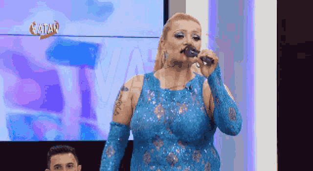 a woman in a blue dress is singing into a microphone with the word batan on the screen behind her