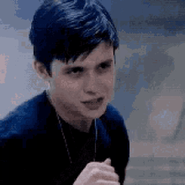 a young man with blue hair is wearing a black shirt and necklace .