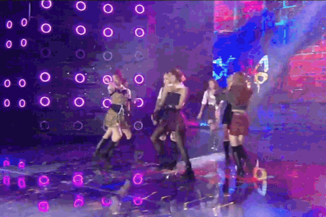 a group of women dancing on a stage with purple lights