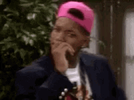 a man wearing a pink baseball cap and a suit is covering his mouth with his hand .