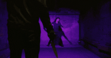 a man in a black shirt is dancing in a dark room with purple lights .