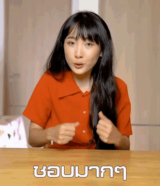 a woman in a red shirt is sitting at a table with a foreign language written on the table in white letters