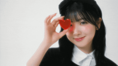 a girl is holding a heart in front of her eye