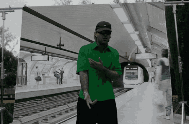 a man in a green shirt stands in front of a subway station