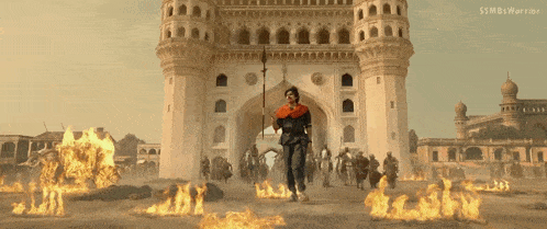 a man holding a sword stands in front of a castle with flames surrounding him