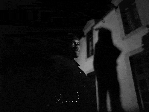 a black and white photo of a woman standing in front of a building .