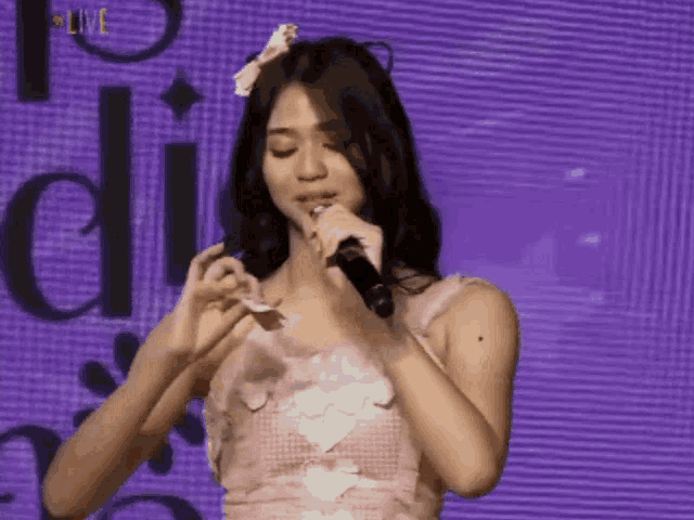 a woman in a pink dress singing into a microphone with the word live in the corner