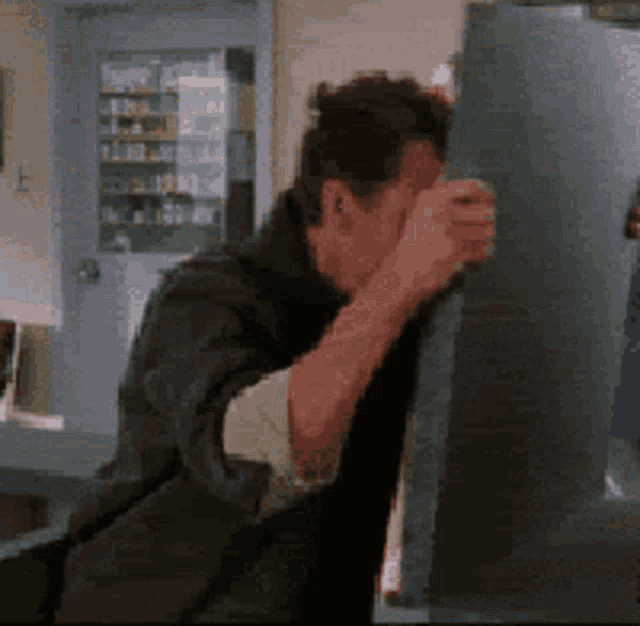 a man covering his face with his hand while standing next to a fridge