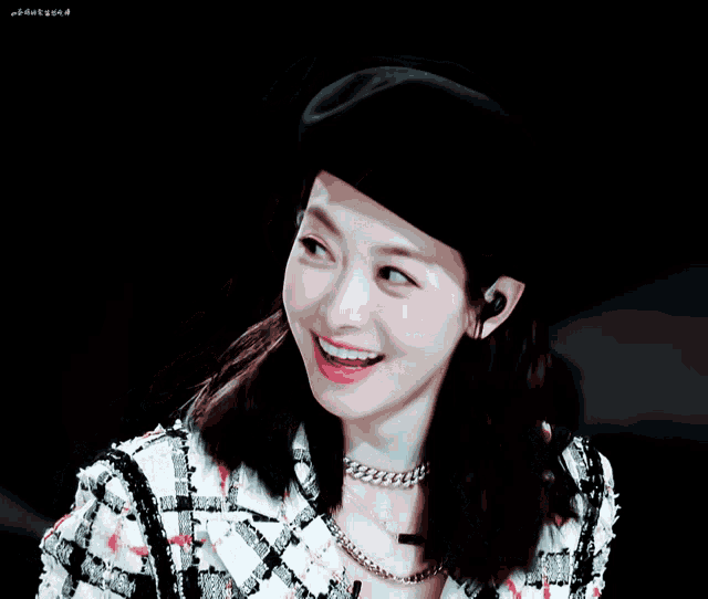 a woman wearing a black beret and a plaid jacket smiles with her eyes closed